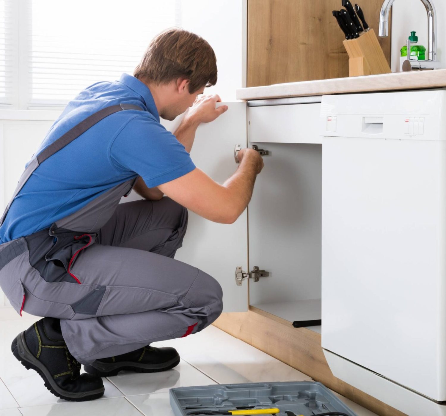 Repairman In Overalls Repairing Cabinet Hinge In Kitchen